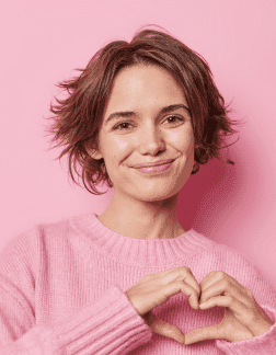 The girl smiles and shows a heart gesture with her hands